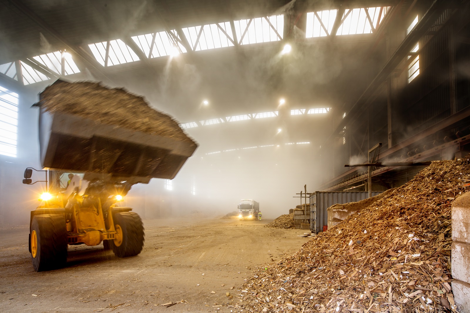 Shovel rijdt met afvalhout in de hal van de bio-energiecentrale om dit op de grote hoop met afvalhout te plaatsen