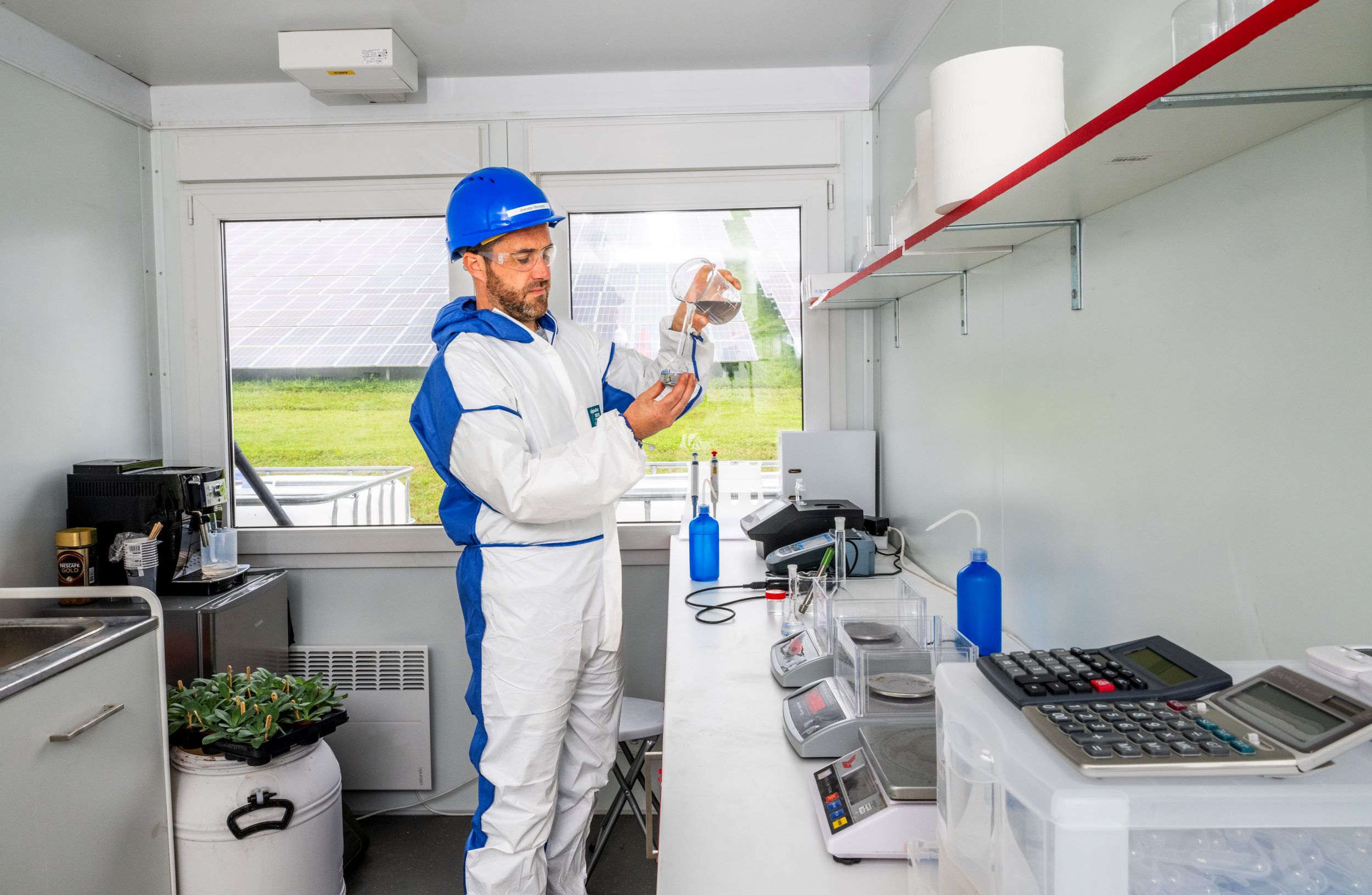 man met helm en pak in lab om fosfaat uit slib te halen