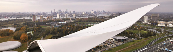 Foto genomen van bovenin een windmolen, uitzicht over Rotterdam en in beeld een wiek.