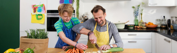 Vader en zoon snijden samen groenten in de keuken om soep te bereiden op elektrische kookplaat.