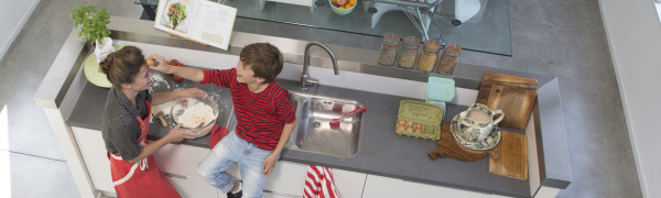 Moeder en zoon maken samen deeg in een witte keuken.