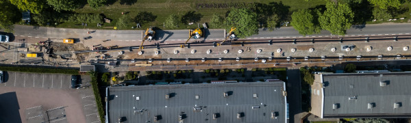 Een foto vanuit de lucht welke de aanleg van ene warmtenet laat zien, de straat ligt open en met kranen worden de warmteleidingen in de grond geplaatst