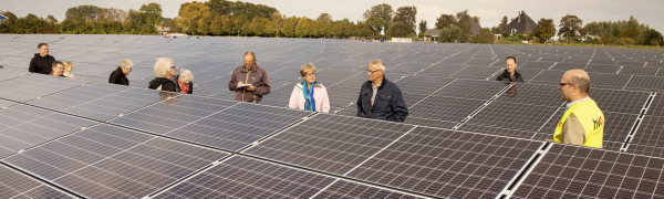 je ziet de zonnepanelen van de zonneweide en daartussen lopen 11 bezoekers van de open dag