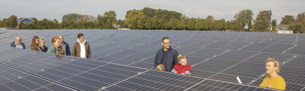 je ziet de zonnepanelen van de zonneweide en daartussen lopen 10 bezoekers van de open dag