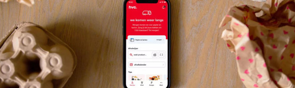 Telefoon met de HVC-app daarop geopend. Daarnaast liggen gepropt papier en een eierdoos