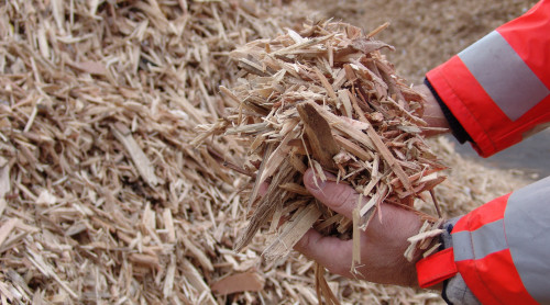 medewerker van HVC raapt met zijn handen houtsnippers op.
