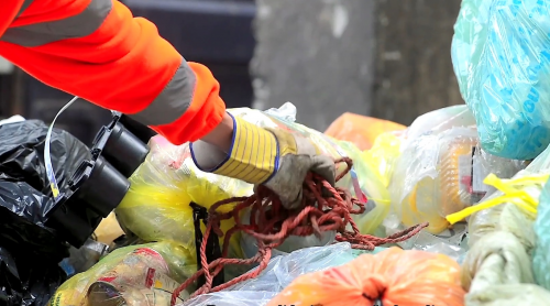 Hand met werkhandschoen grijpt touw tussen balen plastic