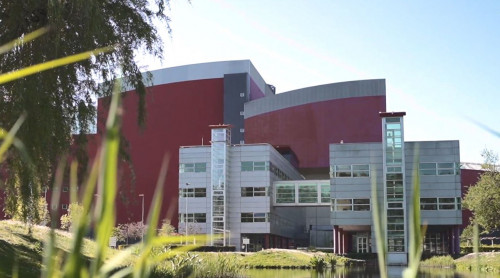 Afbeelding van het HVC kantoor in Alkmaar, op de achtergrond blauwe lucht en op de voorgrond een vijver met groen.