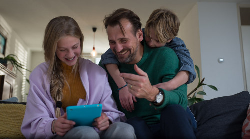 vader en 2 kinderen zitten op de bank en kijken lachend naar een tablet.