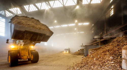 Shovel rijdt met afvalhout in de hal van de bio-energiecentrale om dit op de grote hoop met afvalhout te plaatsen