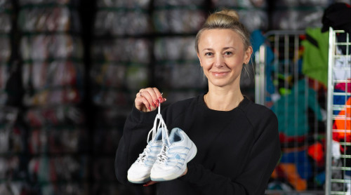 vrouw houdt een paar schoenen vast. Voor haar ligt allemaal textiel. Achter halen staan balen van gesorteerd textiel.