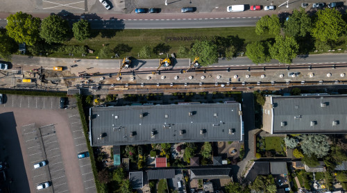 Een foto vanuit de lucht welke de aanleg van ene warmtenet laat zien, de straat ligt open en met kranen worden de warmteleidingen in de grond geplaatst