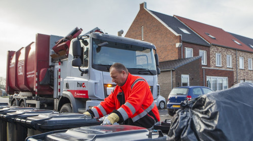Op de voorgrond staan drie grijze bakken. Een chauffeur van HVC pakt met twee handen de tweede bak vast. Op de achtergrond links zie je een zijlader van HVC. Rechts op de achtergrond zie je een blauwe auto en huizen.