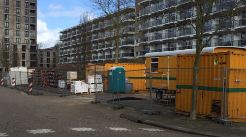 Foto van afgezette parkeerplaats in Sliedrecht, die dient als werkterrein voor de aanleg van het warmtenet. Op de achtergrond flatgebouwen.