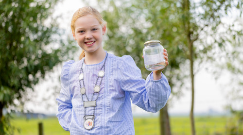 Meisje met burgemeestersketting houdt glazen potje vast in 1 hand.