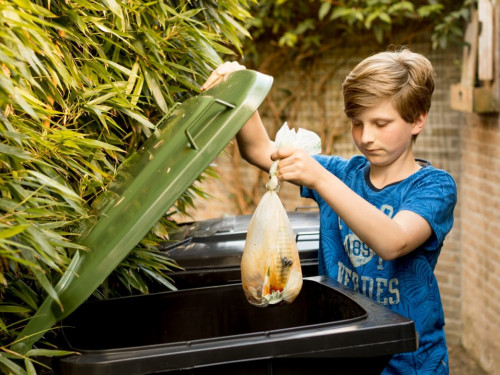 Jongen gooit composteerbaar biozakje in groene container aan huis
