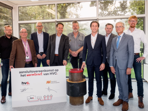 Getekend foambord en stuk van een warmteleiding op de voorgrond en daarachter poseren vertegenwoordigers van Noordwest Ziekenhuisgroep en HVC