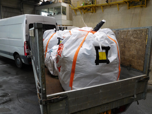Dubbel verpakte zakken van stevig materiaal op een aanhanger achter een wit bestelbusje