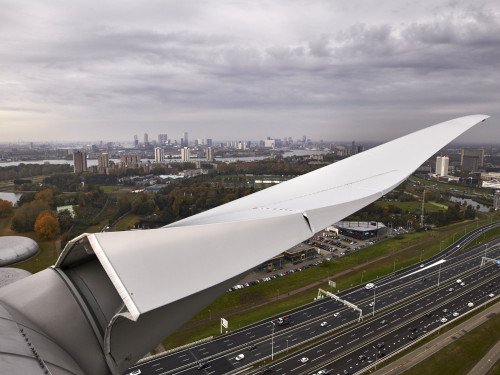 Foto genomen van bovenin een windmolen, uitzicht over Rotterdam en in beeld een wiek.