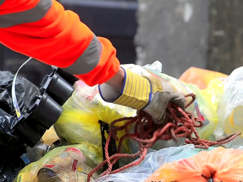 Hand met werkhandschoen grijpt touw tussen balen plastic