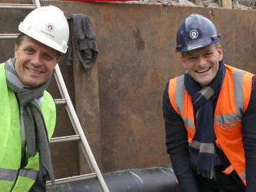 Directeur Ten Elshof en wethouder Van der Linden staan bij warmteleidingen die de grond in gaan