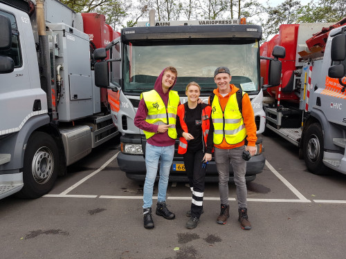 Boaz, Tessa en Enzo staan voor een van de inzamelwagens en kijken glimlachend de camera in