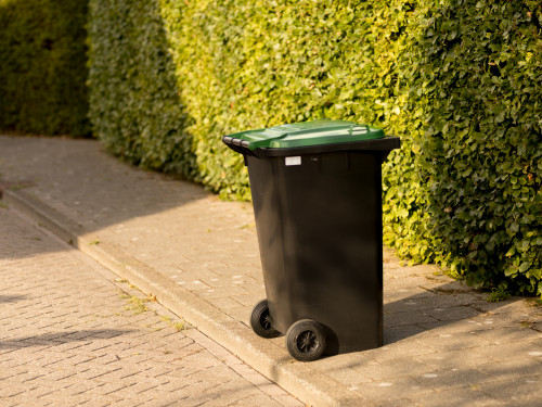 Groene bak met wielen naar de weg toe, klaar om te legen