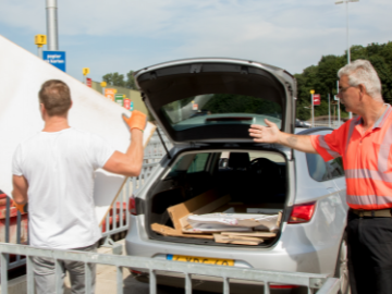 Op het afvalbrengstation wijst een ABS medewerker een bezoeker in welke container een grote witte plaat hoort