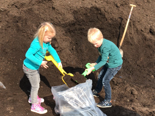 meisje en jongen staan bij een grote composthoop en scheppen compost in doorzichtige zak