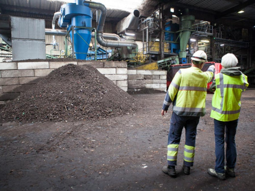 Twee mensen staan in de composteringshal in Middenmeer een van hen wijst naar een installatie en op de voorgrond ligt een hoop compost