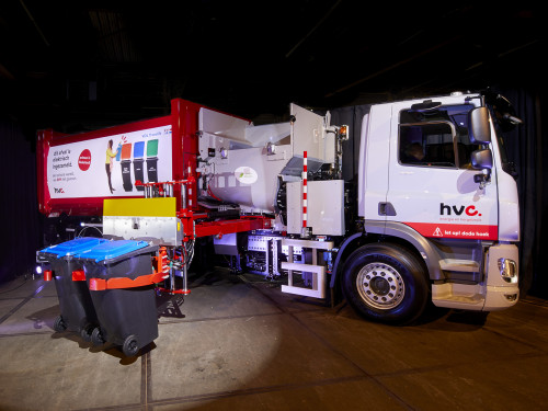 elektrische inzamelwagen pakt twee bakken vast om te gaan legen in de wagen. De bakken staan in de schijnwerpers.