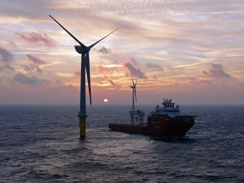 Windmolen op zee op de voorgrond, schip vaart er langs op de achtergrond een ondergaande zon en nog een windmolen in de verte