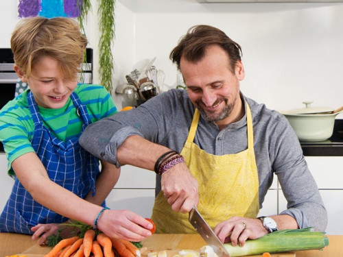Vader en zoon snijden samen groenten in de keuken om soep te bereiden op elektrische kookplaat.