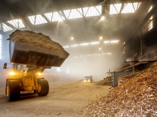 Shovel rijdt met afvalhout in de hal van de bio-energiecentrale om dit op de grote hoop met afvalhout te plaatsen