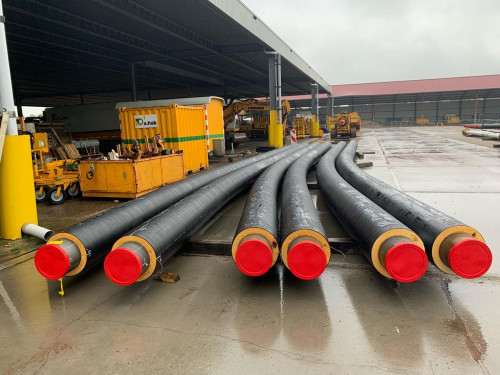 zes warmtebuizen met een rode kop liggen op een bouwterrein. Deze buizen zijn gebogen. De buizen worden gebruikt om het warmtenet aan te leggen. Hierdoor stroomt na de aanleg warm water.