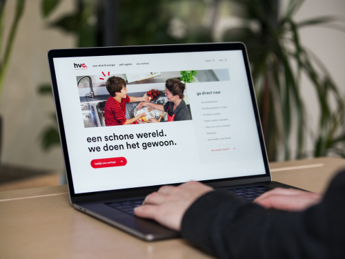 laptop op een tafel, 2 handen die hem bedienen. Op het scherm de HVC homepage en op de achtergrond een plant.