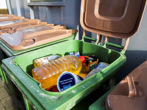 Rij van groene containers, bij één van de groene containers is de klep open en te zien dar daar plastic flessen met frituurvet inzitten.Groene 