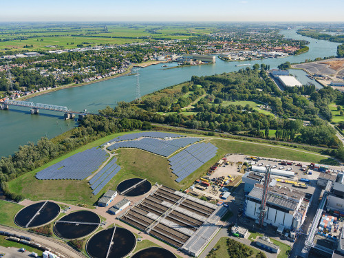 Zonnepanelen op een oude vuilnisbelt gezien vanuit de lucht met op de achtergrond water, waterzuiveringsbasis en de afvalenergiecentrale van HVC