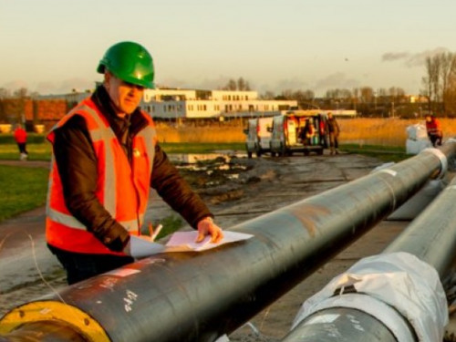 Man staat bij leidingen voor het warmtenet op de achtergrond zie je een molen
