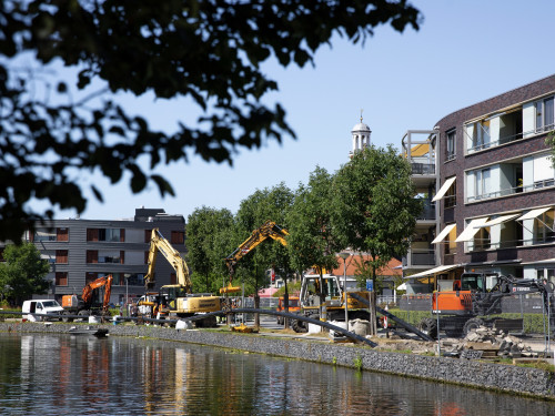 Foto van de aanleg van een warmtenet in Alkmaar, je ziet kranen die de warmteleidingen in de grond leggen en grond afgraven. 