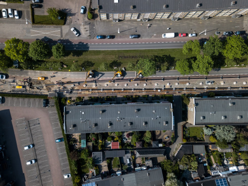 Een foto vanuit de lucht welke de aanleg van ene warmtenet laat zien, de straat ligt open en met kranen worden de warmteleidingen in de grond geplaatst