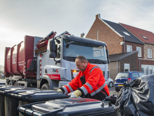 Chauffeur zet de bakken recht voor de wagen. Op achtergrond zie je de wagen en daarachter een rij huizen.