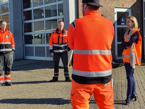 minister Van Veldhoven staat rechts op de foto. OP de rug links van haar staat een chauffeur. Tegenover hem staan nog twee chauffeurs. Op de achtergrond zie je een gebouw