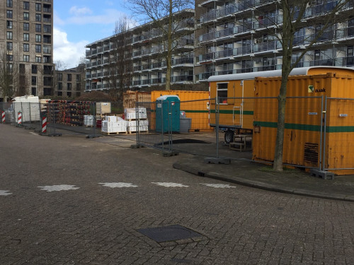 Foto van afgezette parkeerplaats in Sliedrecht, die dient als werkterrein voor de aanleg van het warmtenet. Op de achtergrond flatgebouwen. 