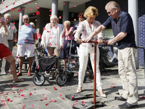Op de foto zie je feestelijke opening van aansluiting op het warmtenet, je ziet bewoners samen de ondergrondse warmtekraam openzetten.