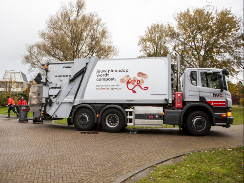 Wagen staat klaar om bakken te legen. Twee chauffeurs brengen de bakken naar de wagen. Een meneer komt nog snel zijn bak brengen om te legen.