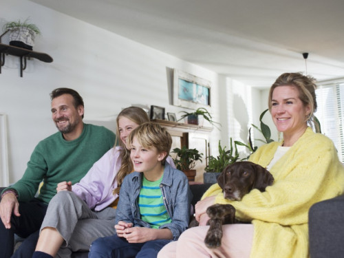 Gezin zit op bank, met twee kinderen en hond op schoot