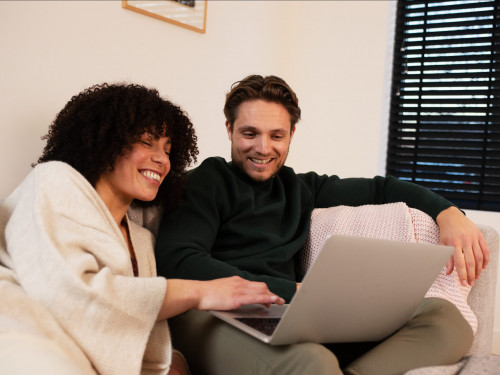 Man en vrouw zitten op de bank en kijken lachend naar beeldscherm van laptop