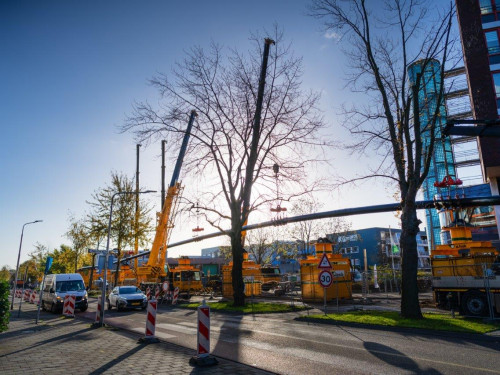 Foto van de werkzaamheden op de Deltalaan waarbij een lange leiding van 540 opgetild wordt door vier grote hijskranen