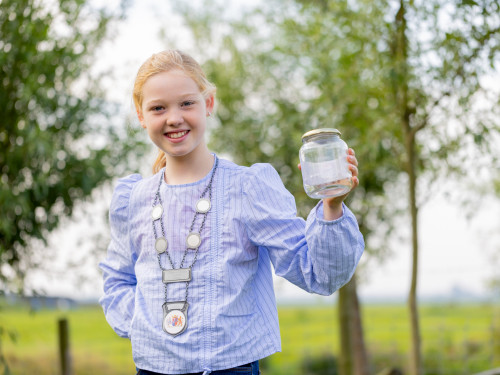 Meisje met burgemeestersketting houdt glazen potje vast in 1 hand.